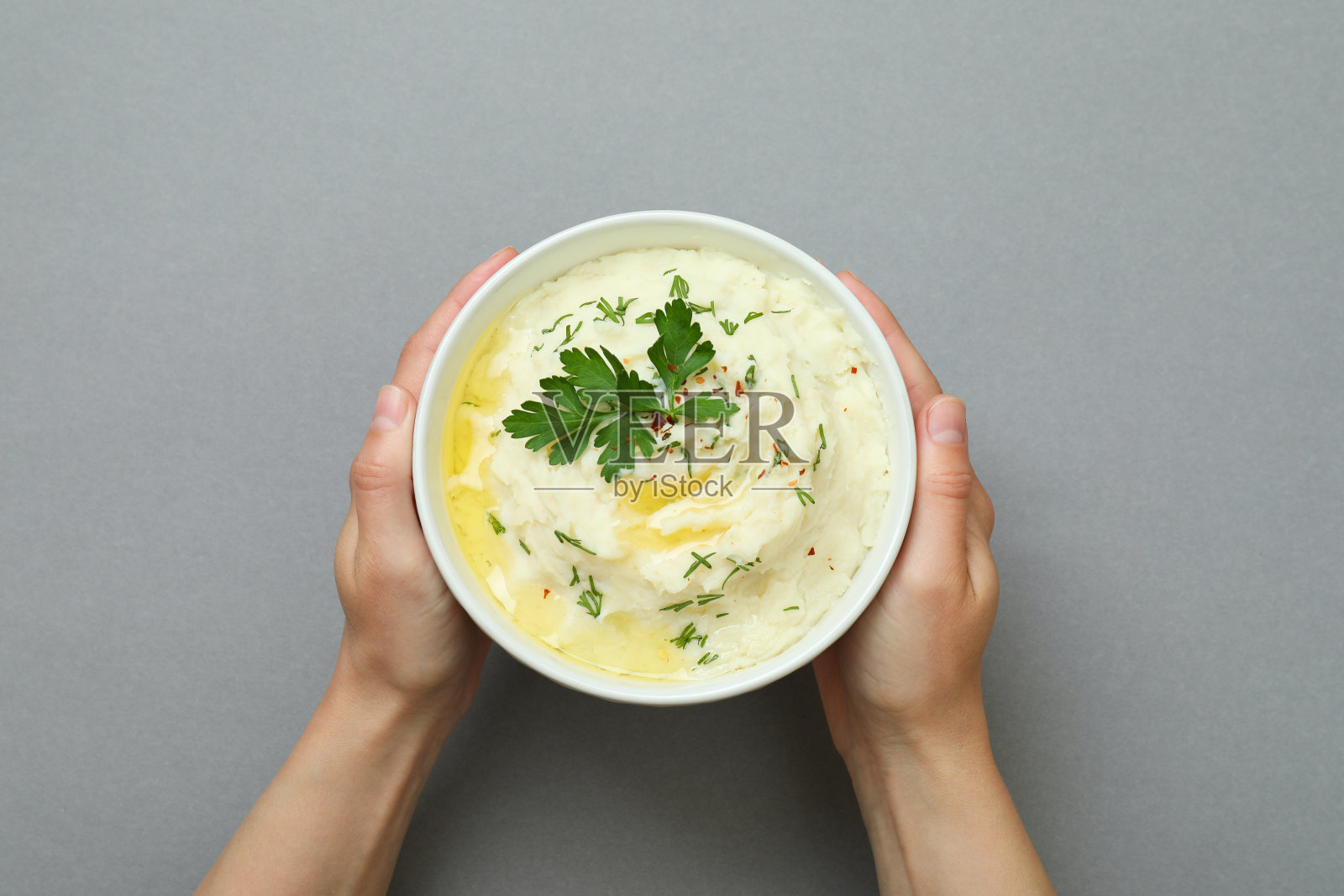 女人的手拿着一碗灰色背景的土豆泥照片摄影图片