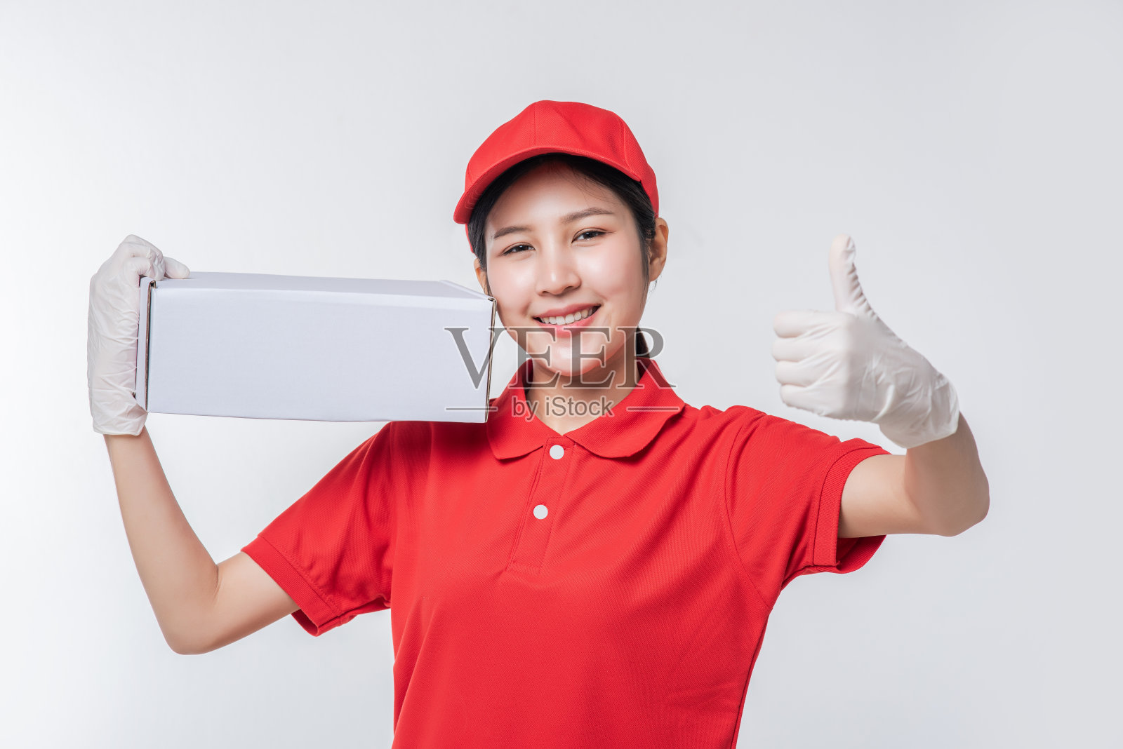 年轻的送货员在红色帽子空白t恤制服站与空白色纸箱孤立在浅灰色背景工作室的形象照片摄影图片