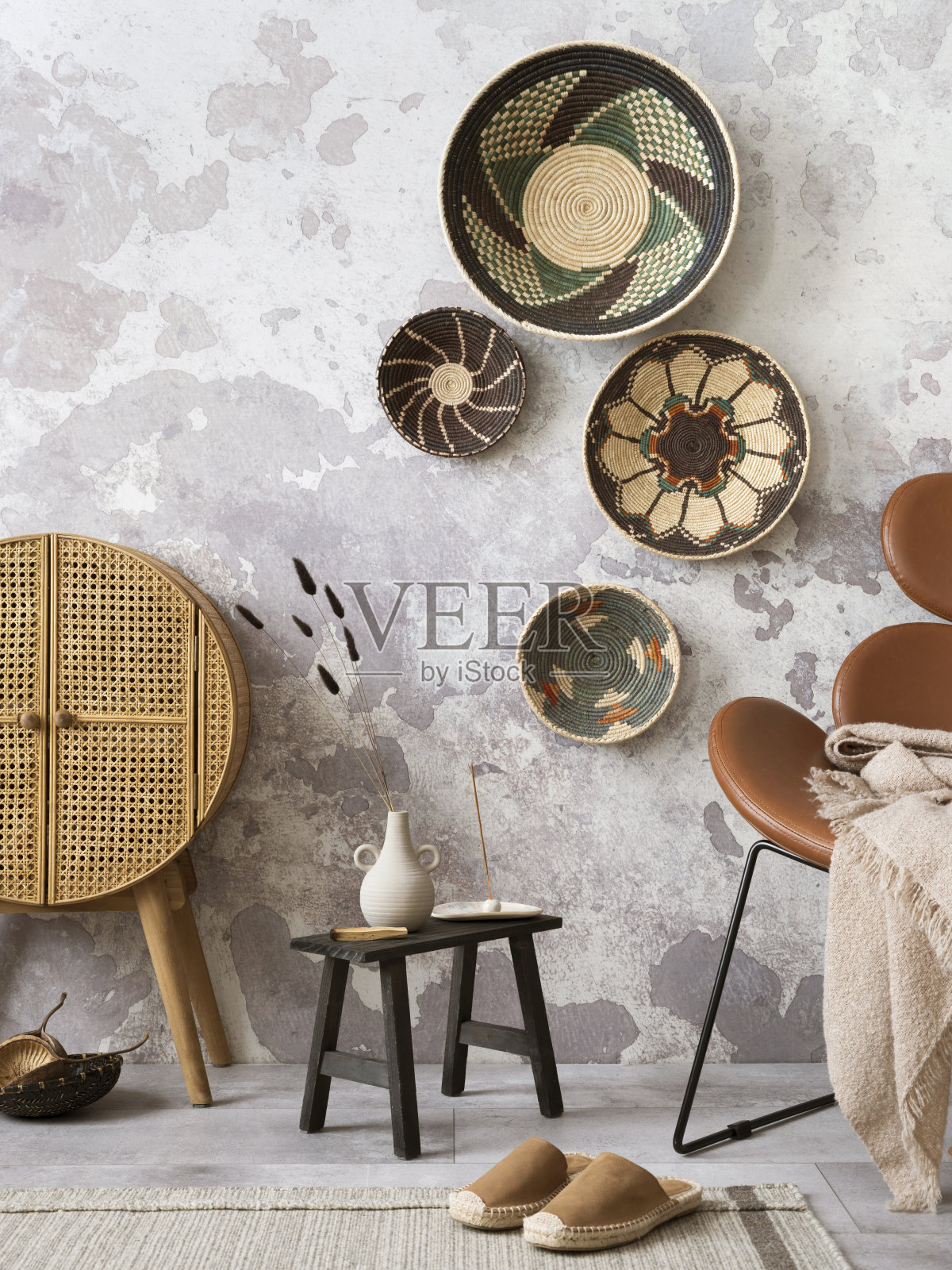 富有创意的民族风格客厅内饰，色彩鲜艳的篮子，藤条餐具柜，棕色扶手椅和优雅的个人配饰。灰色的混凝土墙。家居装饰。模板。照片摄影图片