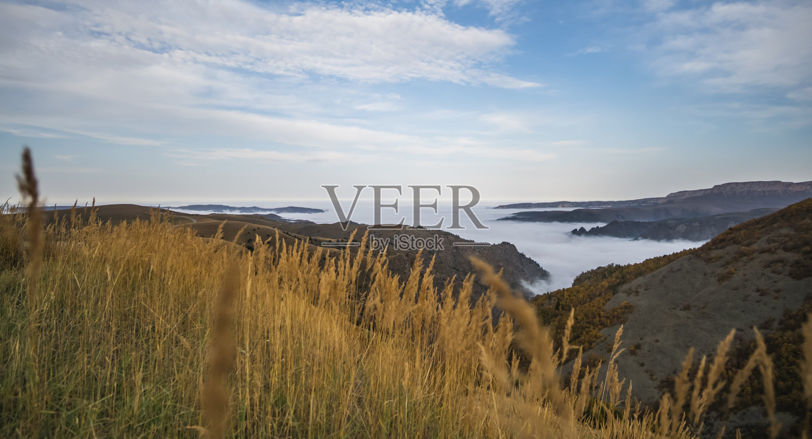 雾和云沿着山谷的底部蔓延，在高加索山脉，秋天长满了植被和枯黄的草照片摄影图片