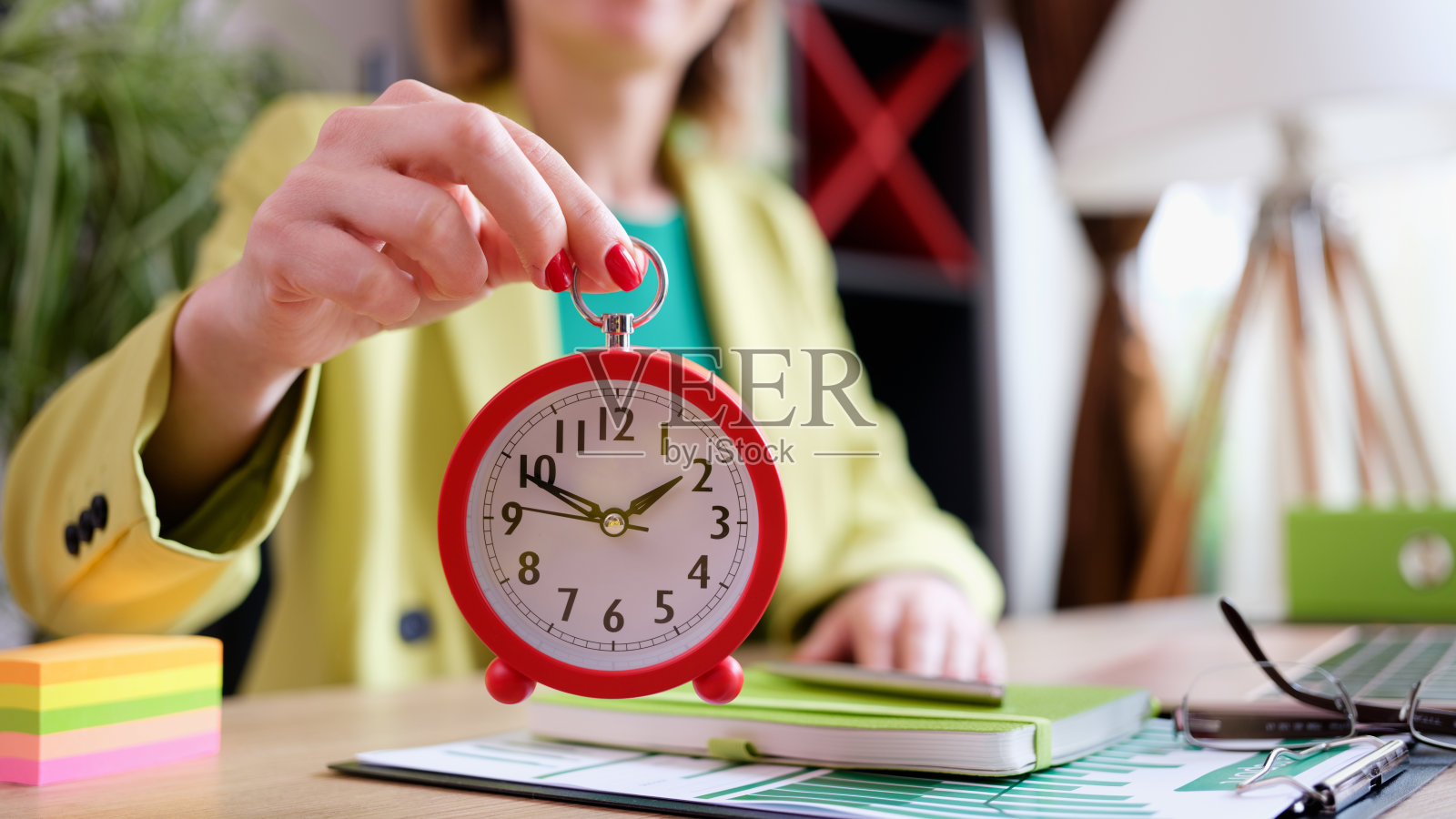 女商人拿着红色的闹钟在工作场所照片摄影图片