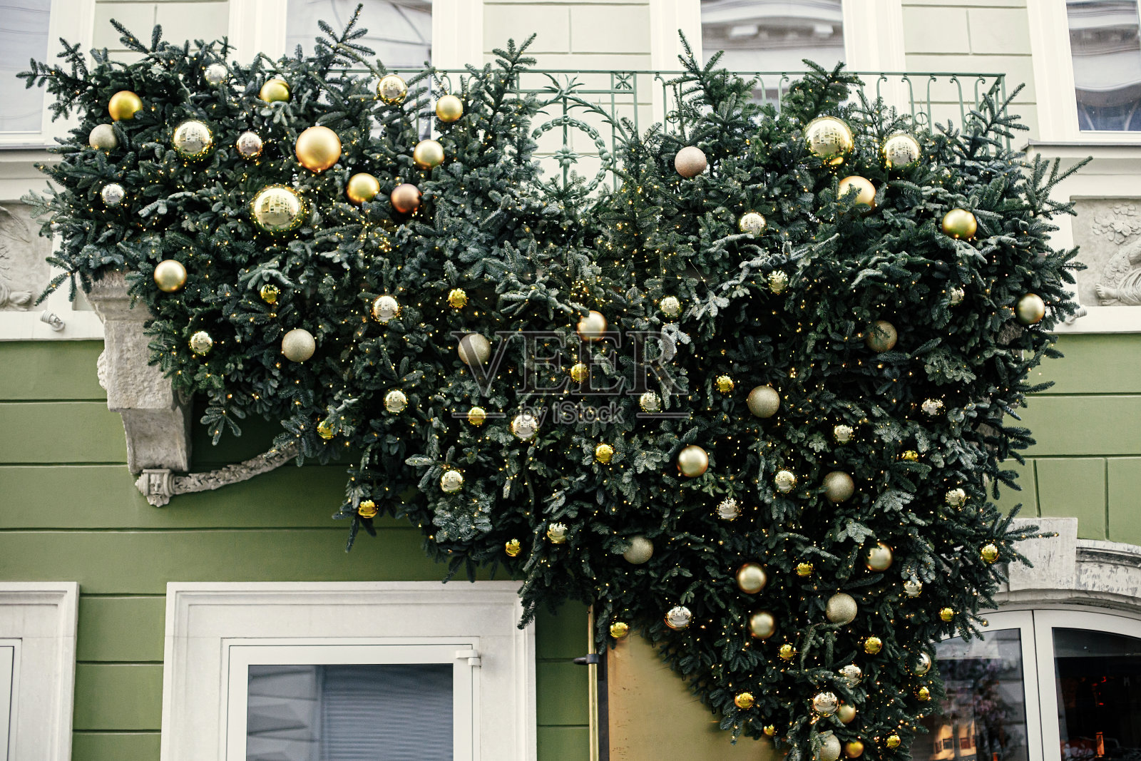 时尚的圣诞杉木树枝与绿色和金色的小玩意和灯的建筑外观。城市街道上的现代圣诞装饰。在欧洲度寒假。圣诞快乐照片摄影图片