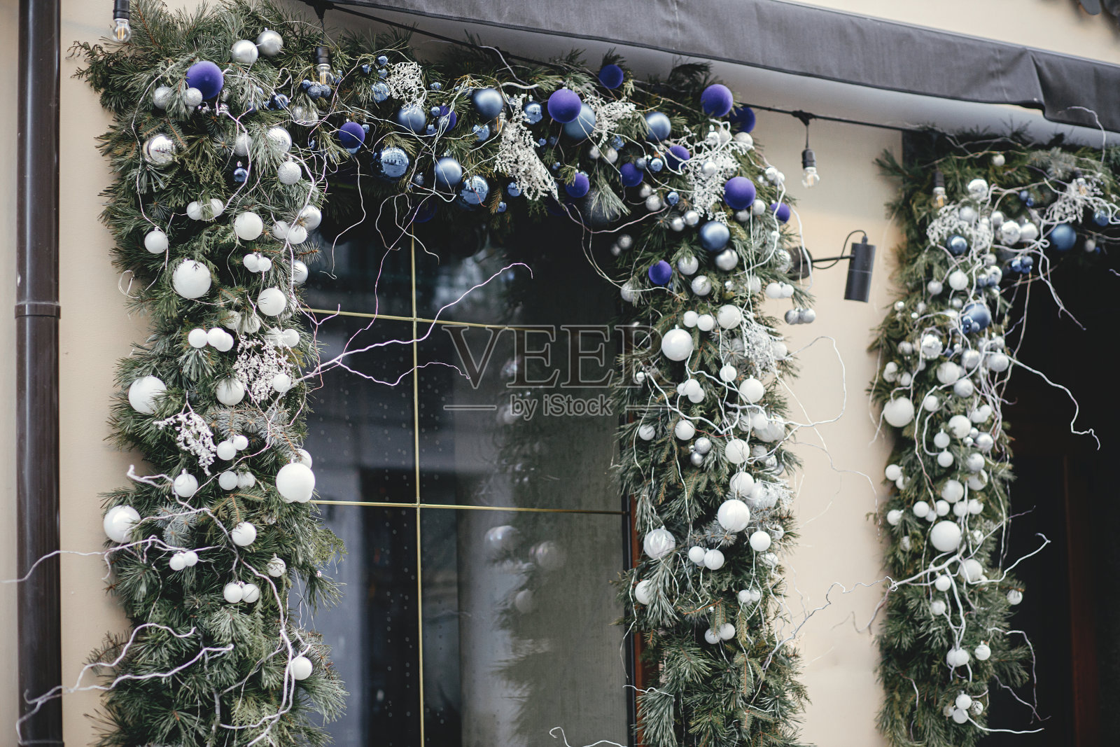 时尚的圣诞银色和蓝色小玩意和杉木树枝在建筑外部。城市街道上的现代圣诞装饰。在欧洲度寒假。圣诞快乐照片摄影图片