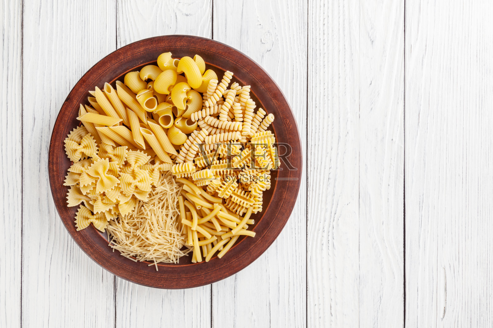 不同类型和形状的意大利面食在陶瓷盘子上的白色木制背景照片摄影图片