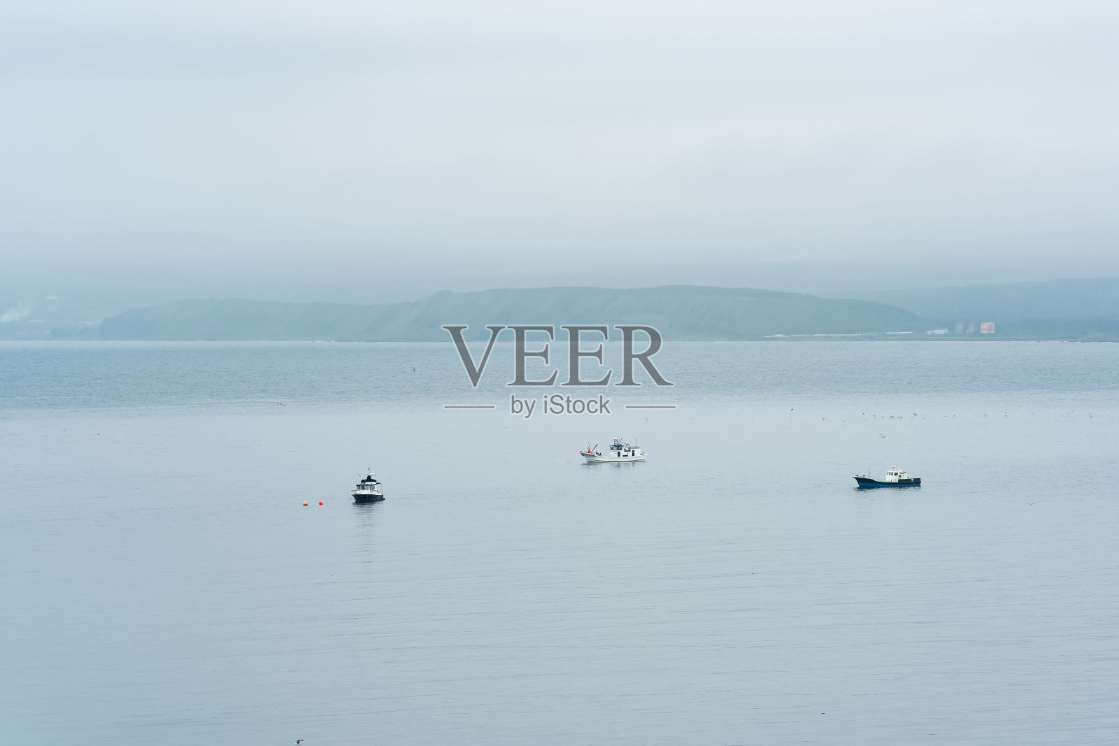 远处雾蒙蒙的海岸映衬着海上的渔船照片摄影图片