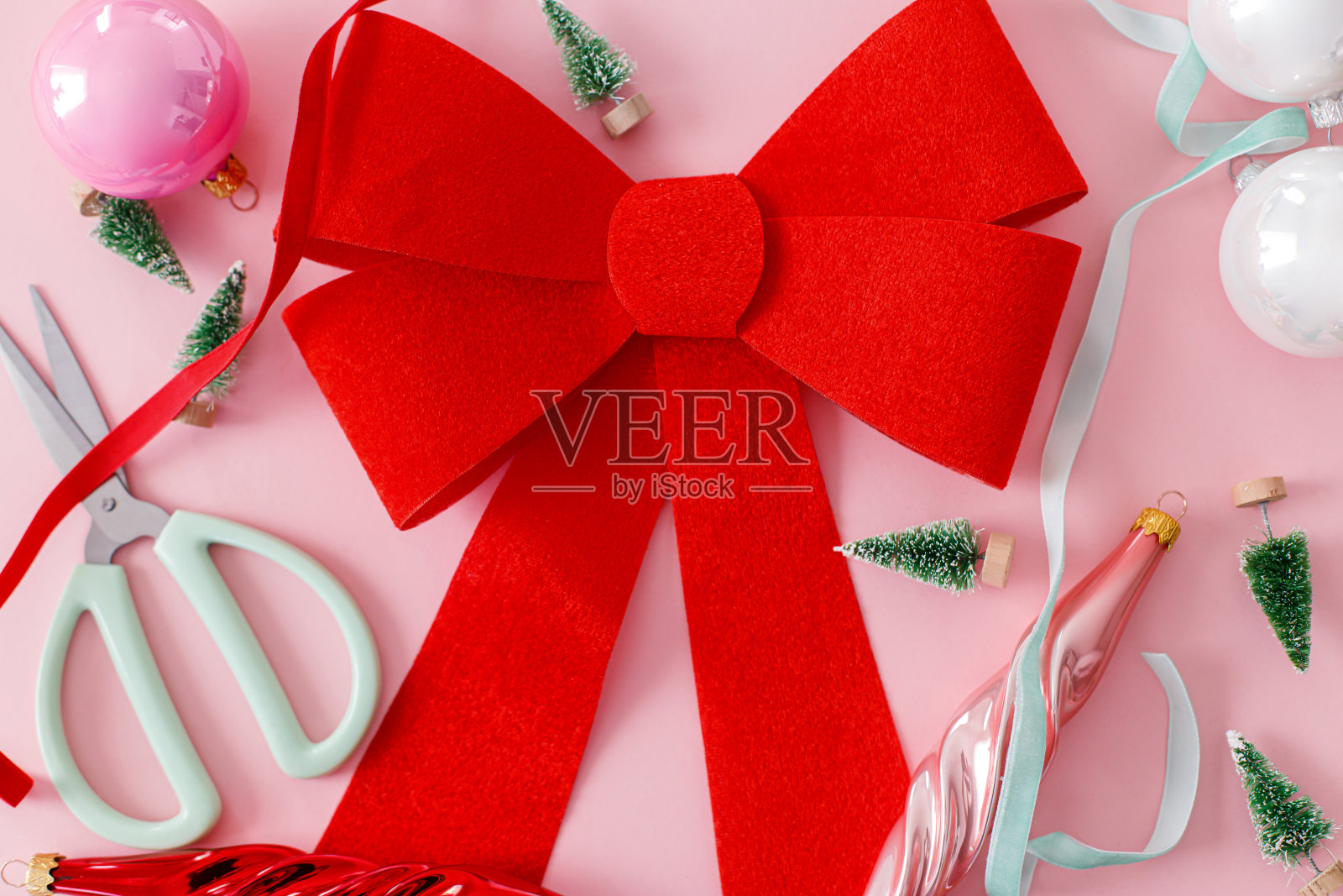寒假的概念。时髦的红色蝴蝶结，装饰物，小绿树，粉色背景上的丝带。创意粉色圣诞构图。圣诞快乐，节日快乐!照片摄影图片