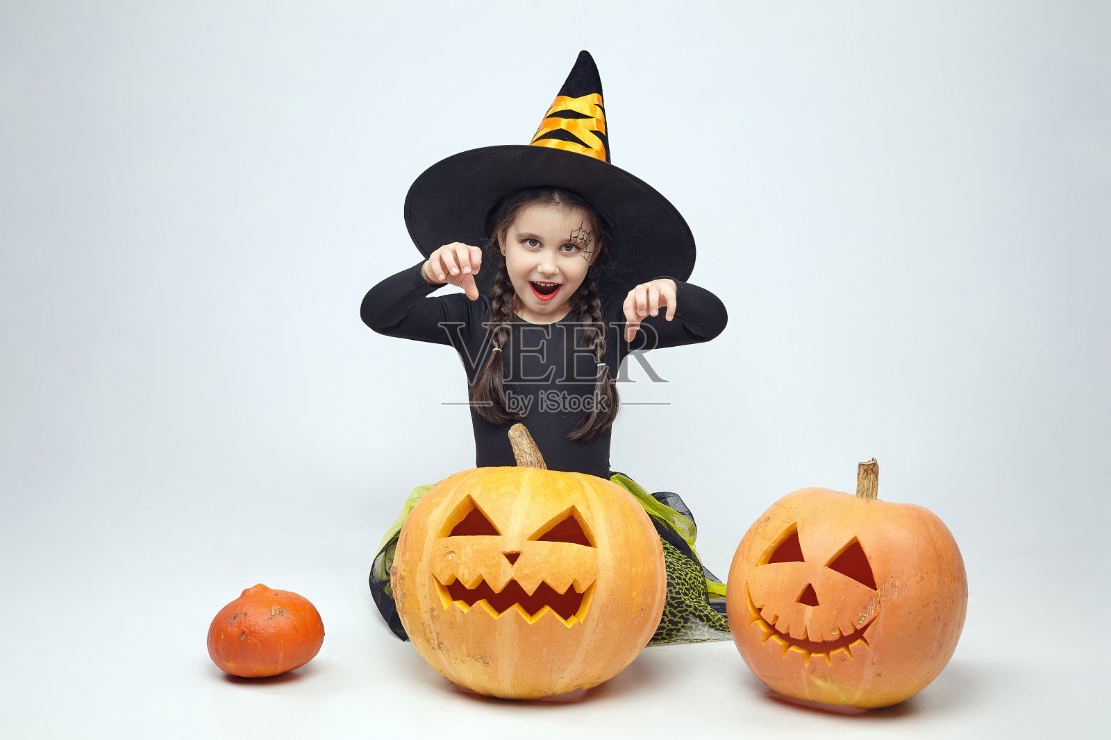 一个穿着女巫服装的迷人小女孩的肖像，杰克的灯站在周围。春节的概念照片摄影图片