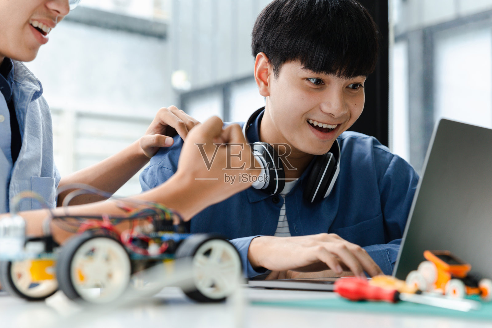 两个亚洲青少年在科学教室用笔记本电脑制作机器人手臂项目。照片摄影图片