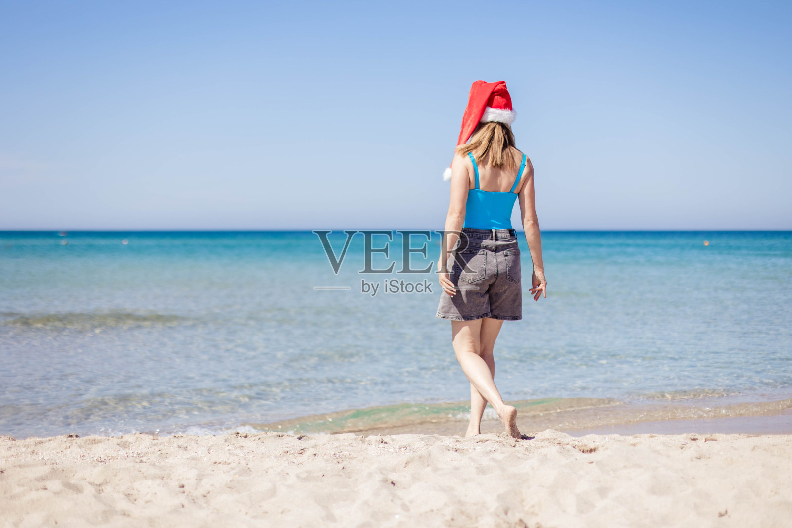 一个年轻的女人戴着圣诞老人的帽子沿着大海或海洋散步，圣诞和新年的概念照片摄影图片