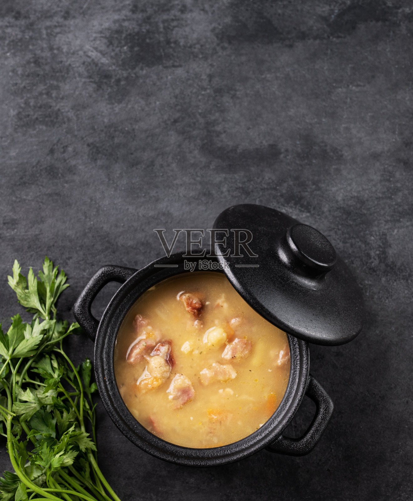 豌豆汤与烟熏火腿在黑色的炖锅深色背景香草。照片摄影图片