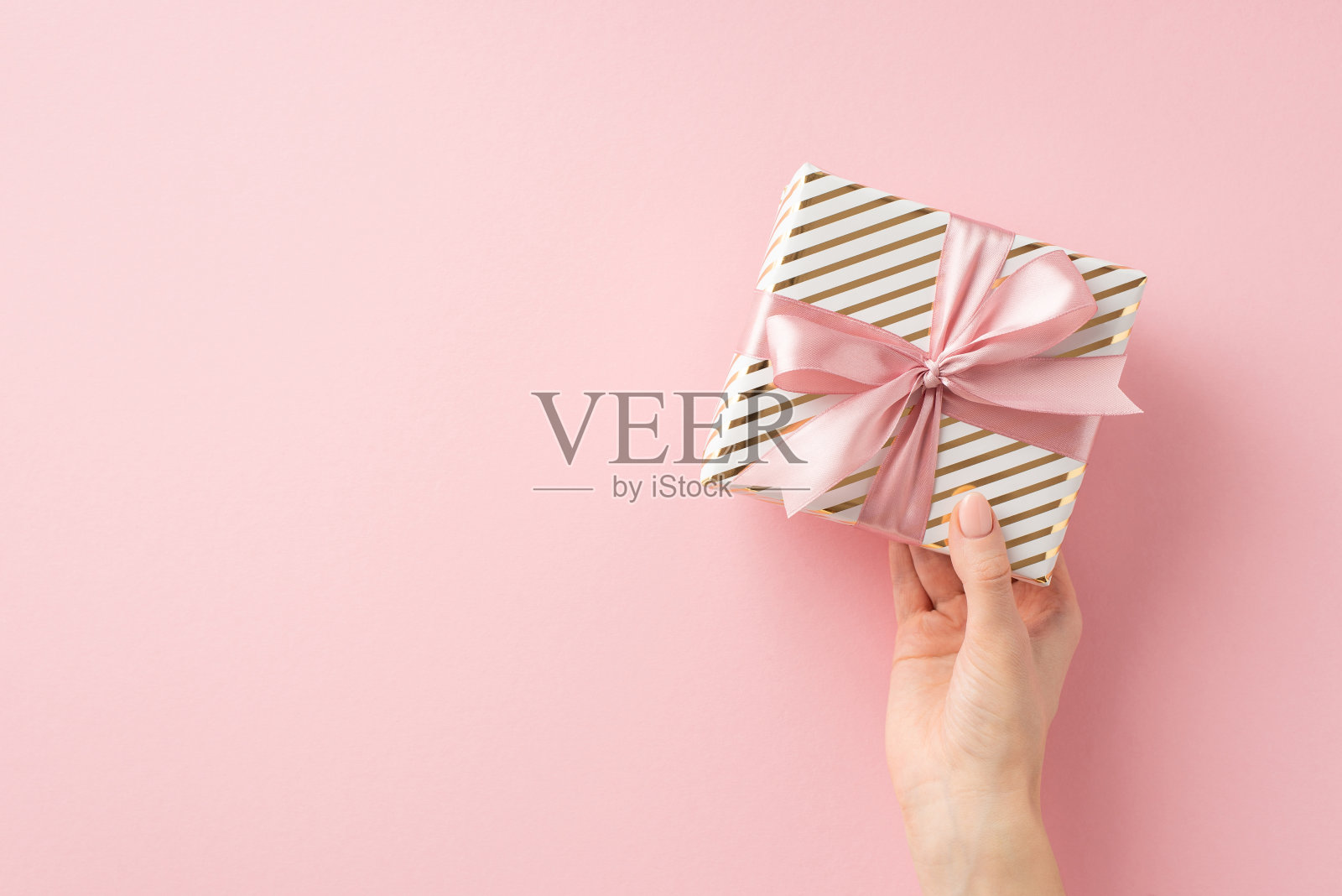 圣诞夜庆祝概念。第一人称俯视图照片的妇女手握时尚的礼物盒与粉色丝带蝴蝶结上孤立的浅粉色背景与copyspace照片摄影图片