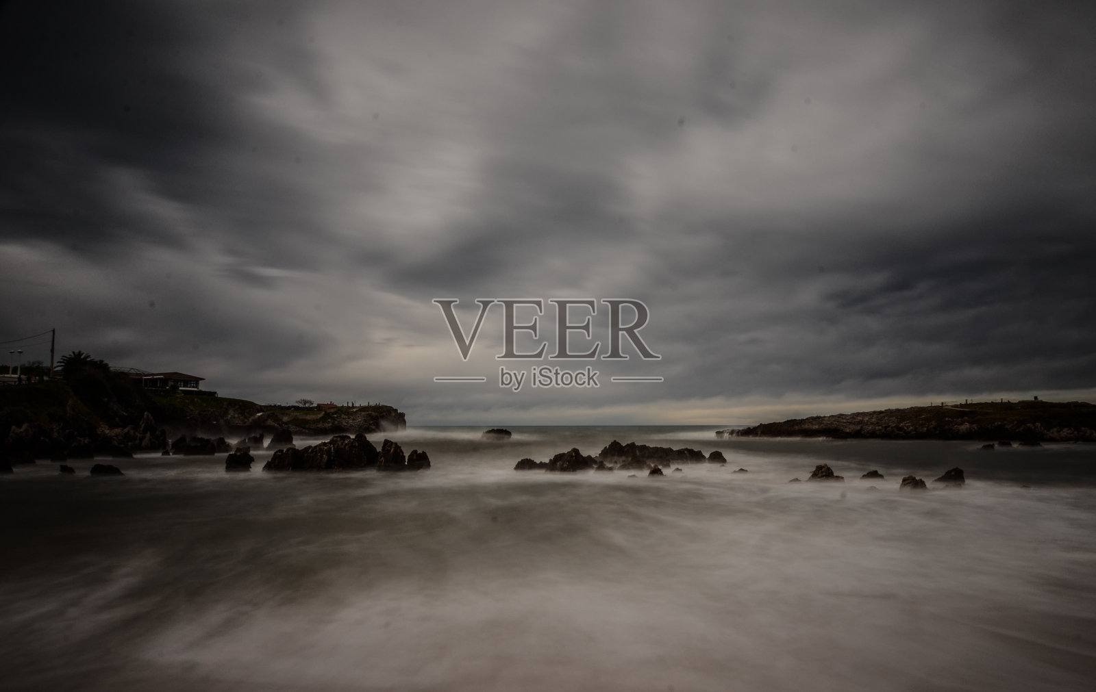 在一个阴沉的日子里，被悬崖和众多岩石包围的海边的长曝光镜头照片摄影图片