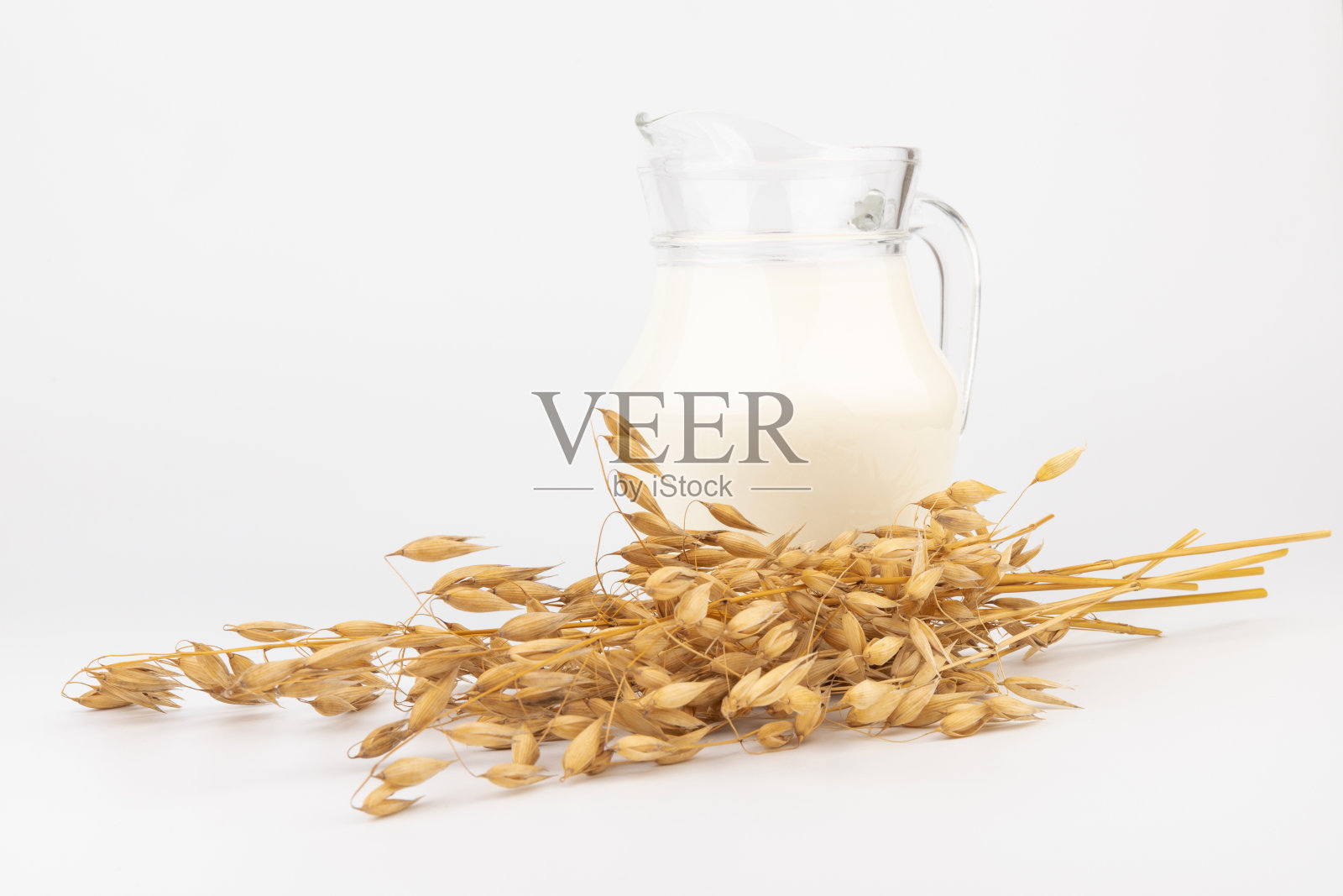 燕麦牛奶在玻璃罐和燕麦穗在光背景。纯素非乳制品替代牛奶。照片摄影图片