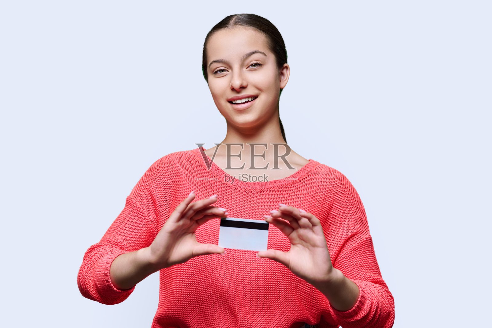 十几岁的学生女孩展示银行信用卡，在白色的工作室背景照片摄影图片