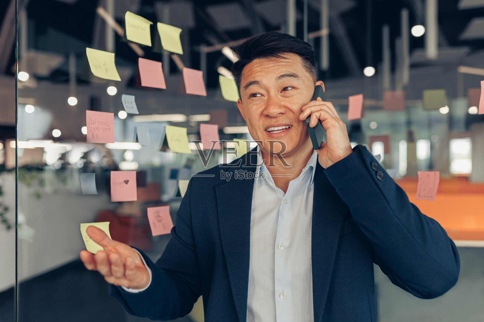 忙碌的亚洲商人西装革履，站在现代办公环境中打电话照片摄影图片