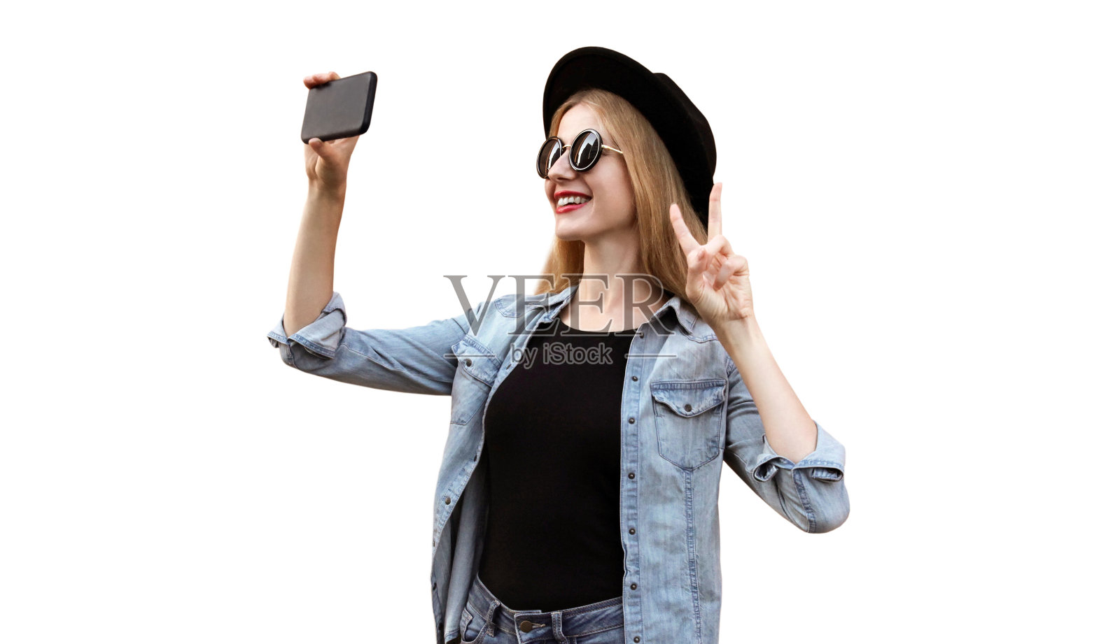 照片中快乐微笑的年轻女子正在用智能手机自拍，戴着白色背景的黑色圆帽照片摄影图片