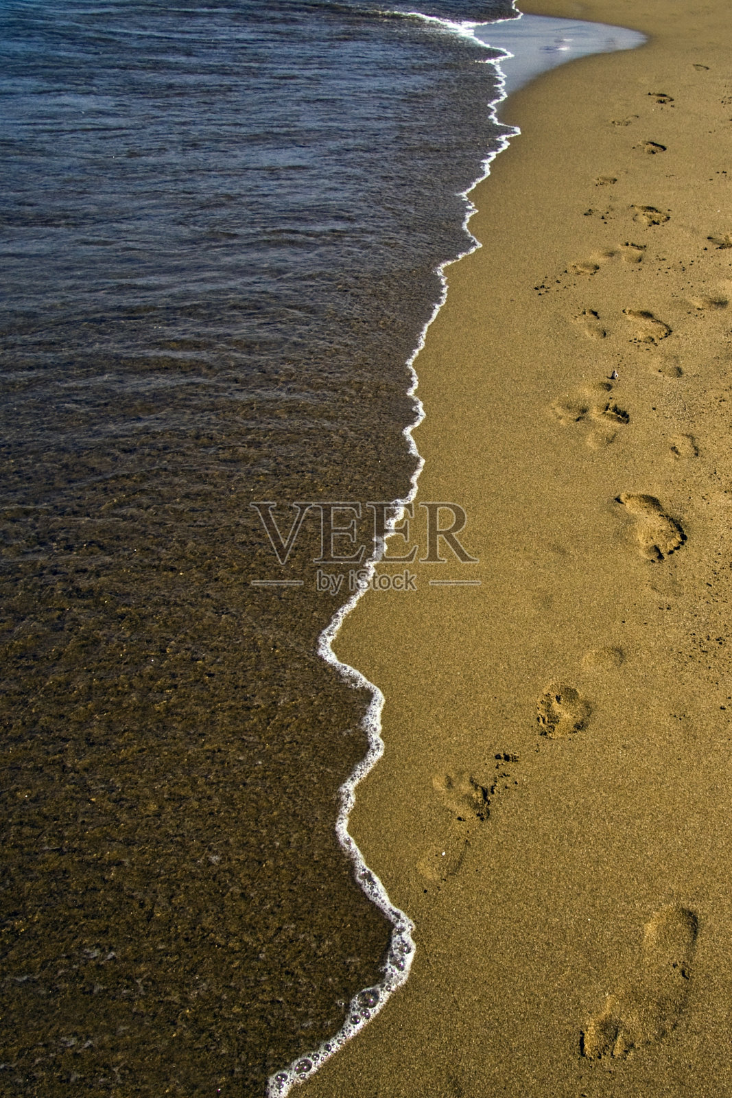 垂直拍摄的一个干净的海滩与脚印和海浪照片摄影图片
