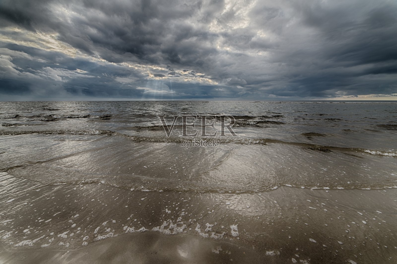 在黑暗的天空下，太阳隐藏在云层后面，沙滩上的美丽照片照片摄影图片