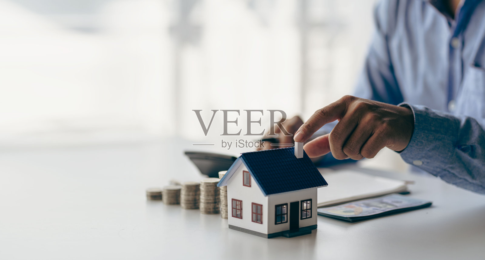 在购买新房之前要检查一下清单，以满足银行的标准。特写镜头的银币下降和房屋模型的储蓄，将你的钱添加到未来概念的房地产业主。照片摄影图片