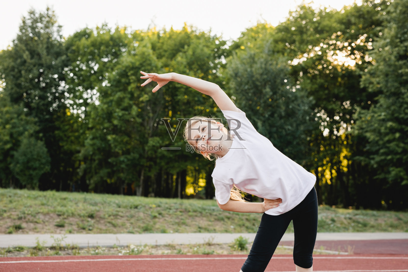 一名小女孩在公园的跑道上跑步前做伸展运动照片摄影图片