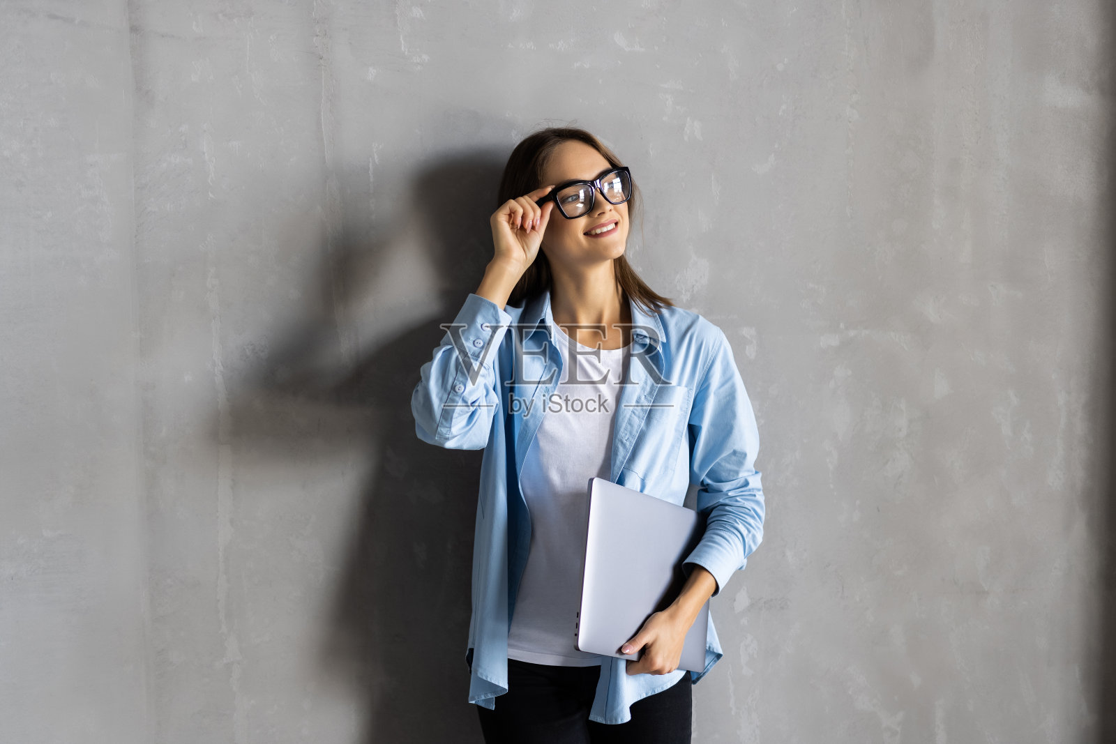 年轻的商业妇女摆出孤立的灰色墙背景坐在凳子上使用笔记本电脑。照片摄影图片