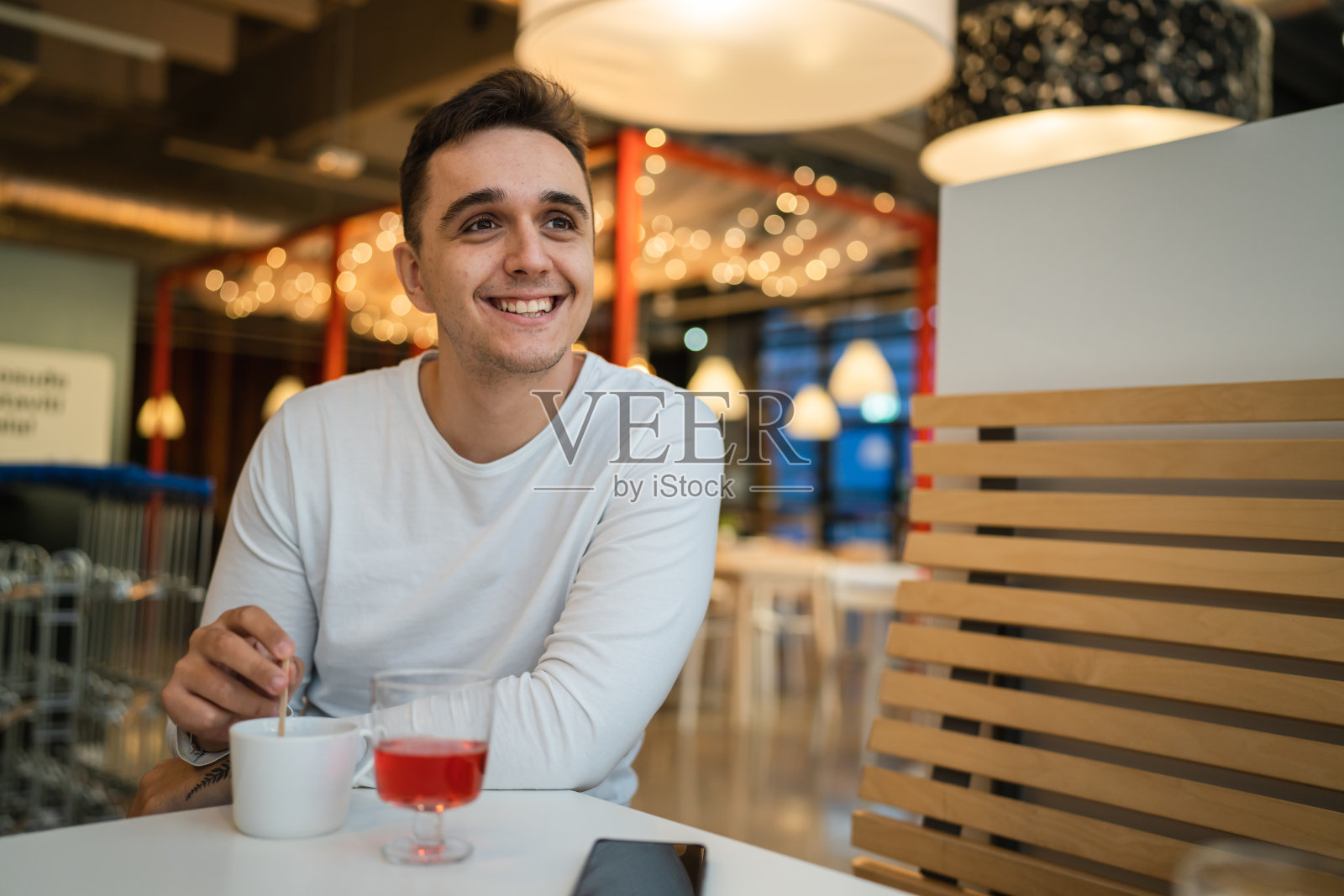 一名年轻的白人男子坐在咖啡馆或餐厅独自看着一边喝着咖啡真实的人复制空间快乐的微笑照片摄影图片