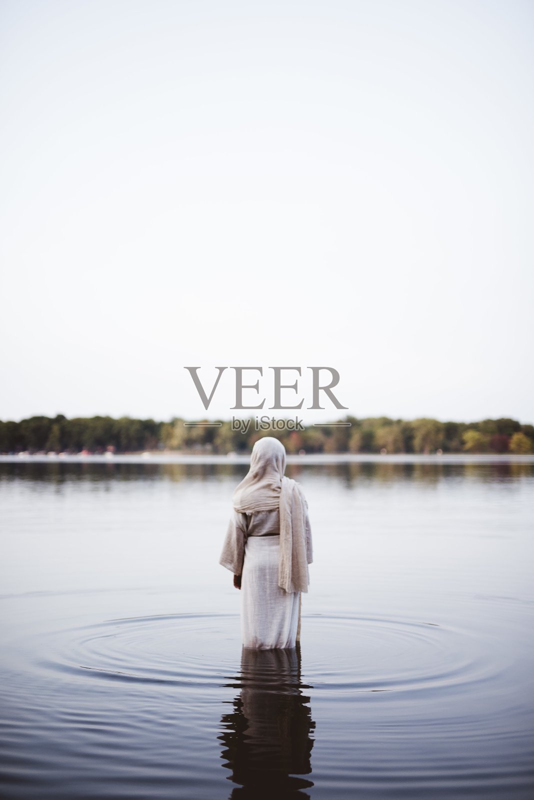 垂直拍摄的女性穿着圣经长袍在水中行走与模糊的背景照片摄影图片