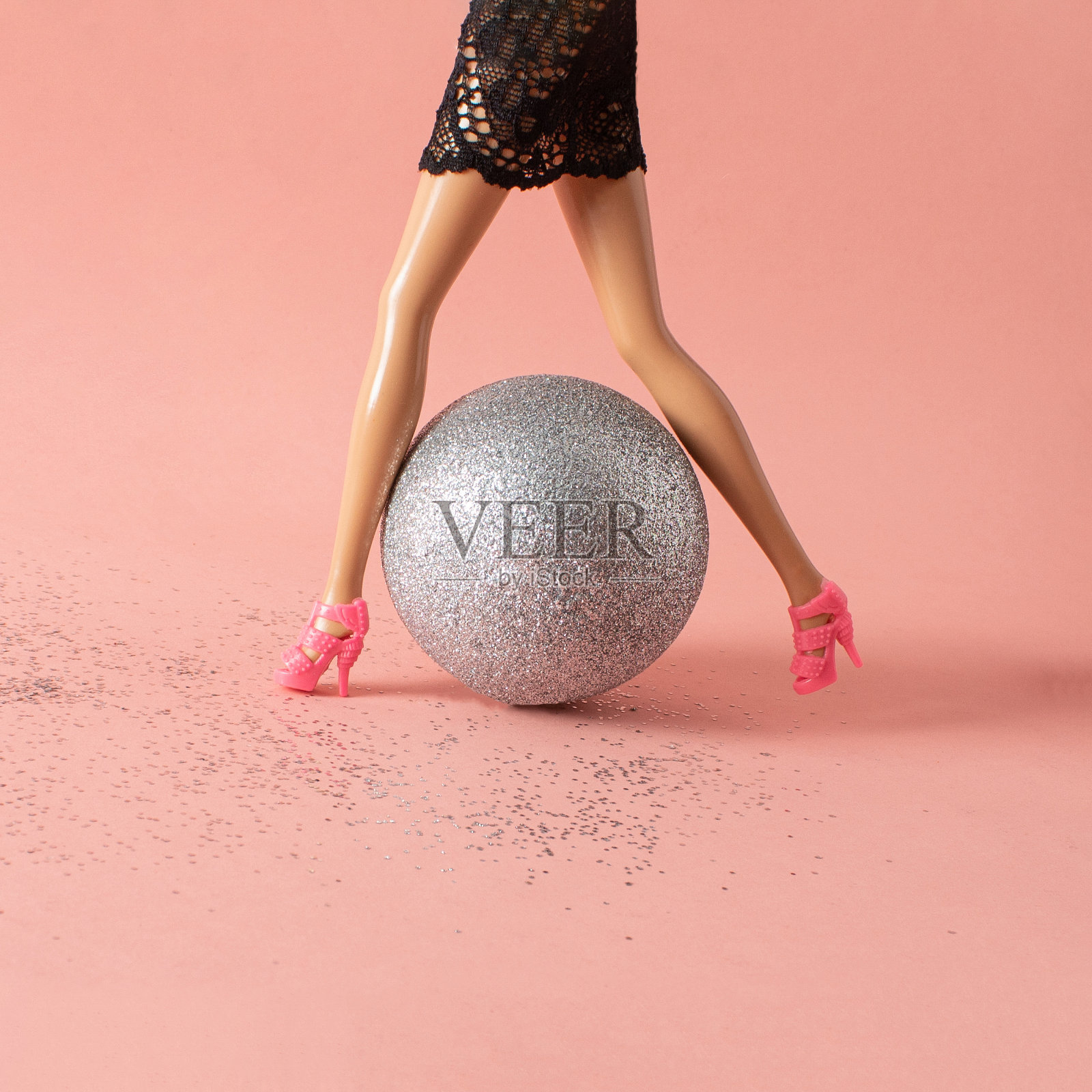 女娃娃的腿和圣诞节闪闪发光的小玩意儿。浅橙色背景上的最小创意概念。照片摄影图片