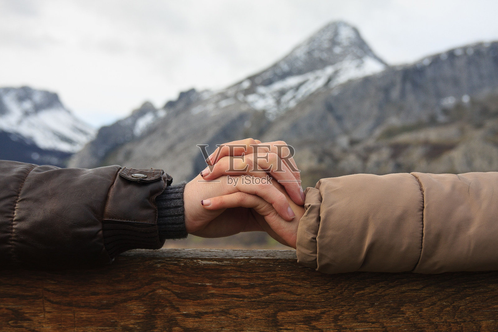 一对情侣手牵着手的浪漫特写镜头，映衬着冬天白雪覆盖的群山照片摄影图片