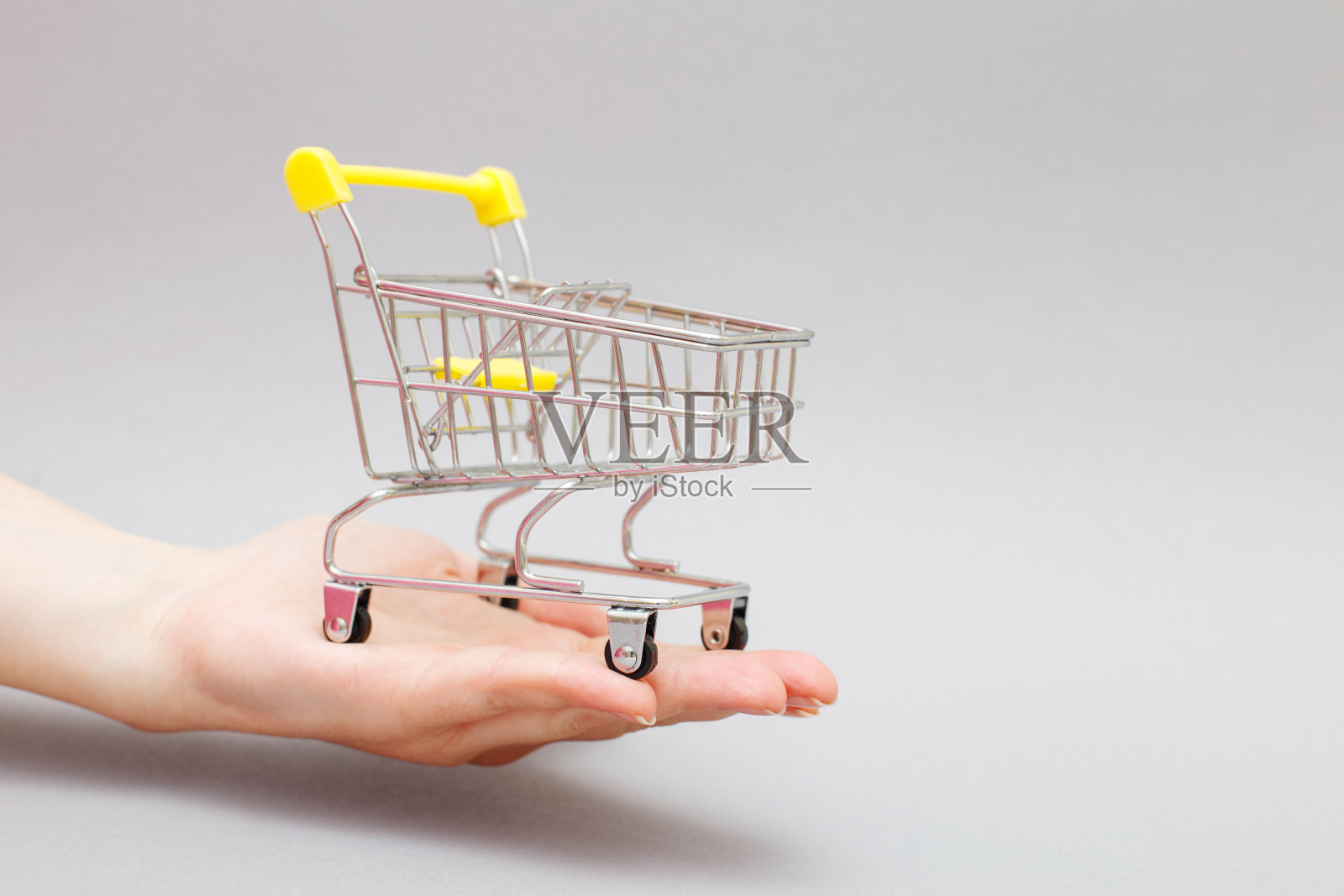 灰色背景下女性手中的购物车。横幅照片摄影图片