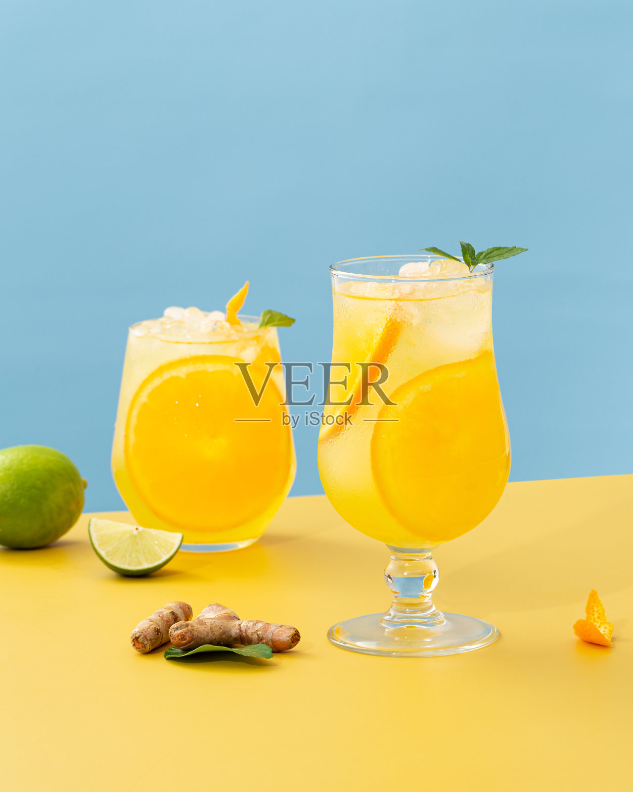 新鲜鸡尾酒的垂直镜头与橙汁在黄色表面与酸橙和姜照片摄影图片