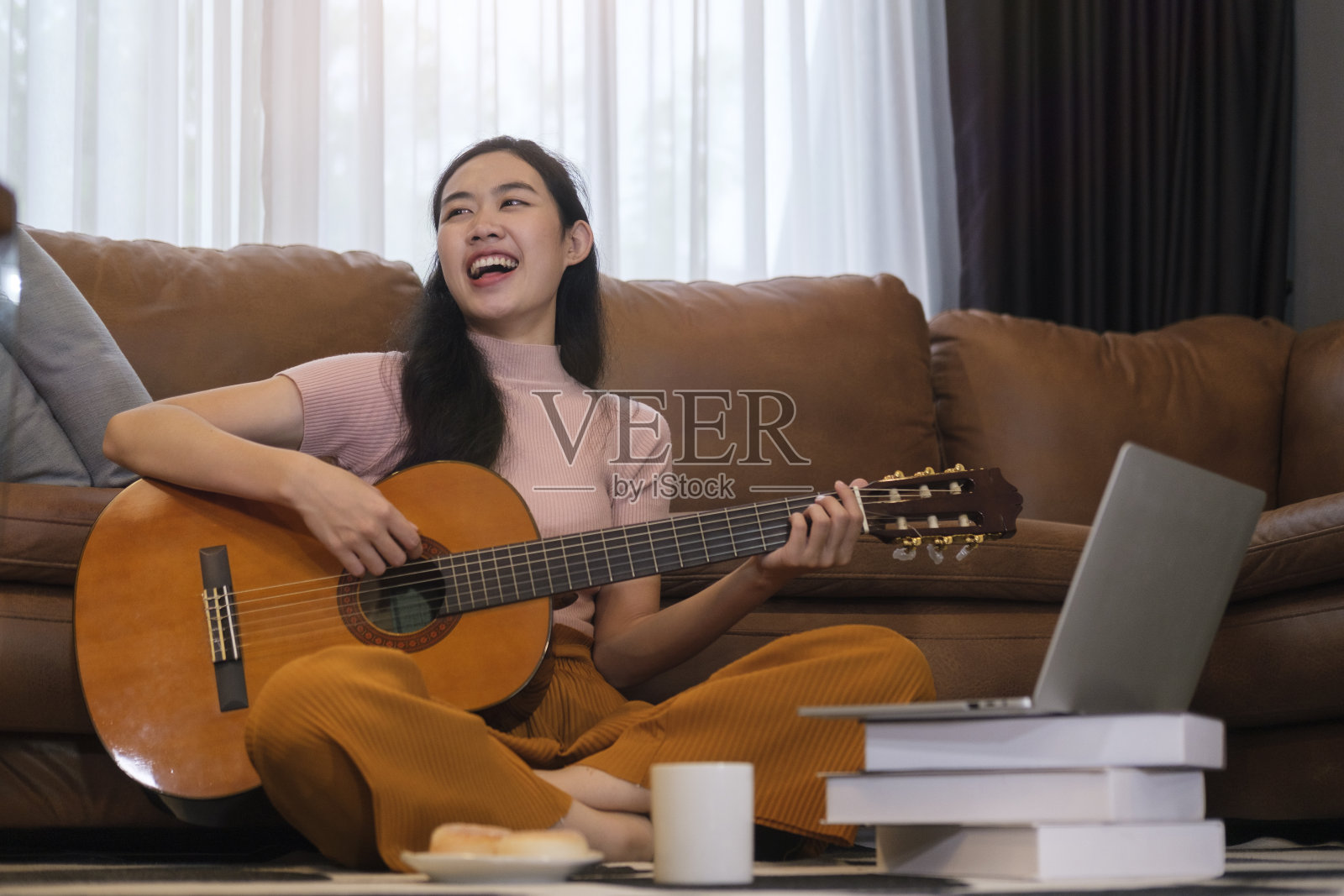 快乐的年轻女子坐在舒适的客厅和弹吉他。照片摄影图片