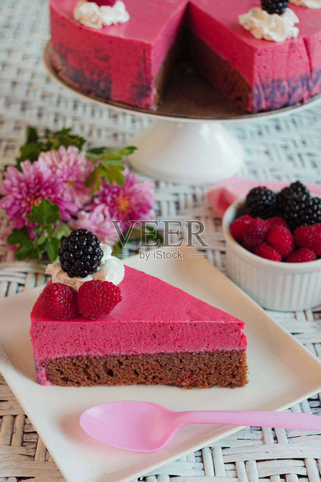 垂直拍摄的黑莓和覆盆子芝士蛋糕与粉红色的勺子在一个正方形的盘子照片摄影图片