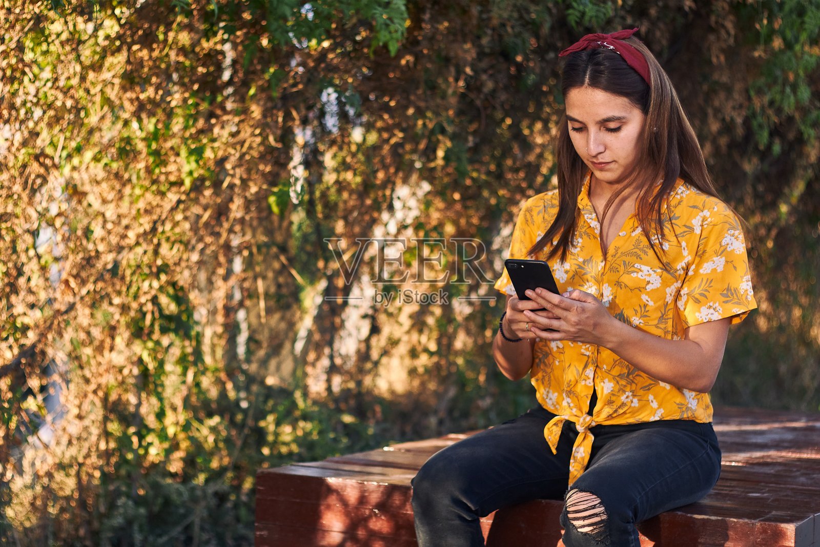 一个小女孩坐在长凳上看手机的镜头照片摄影图片