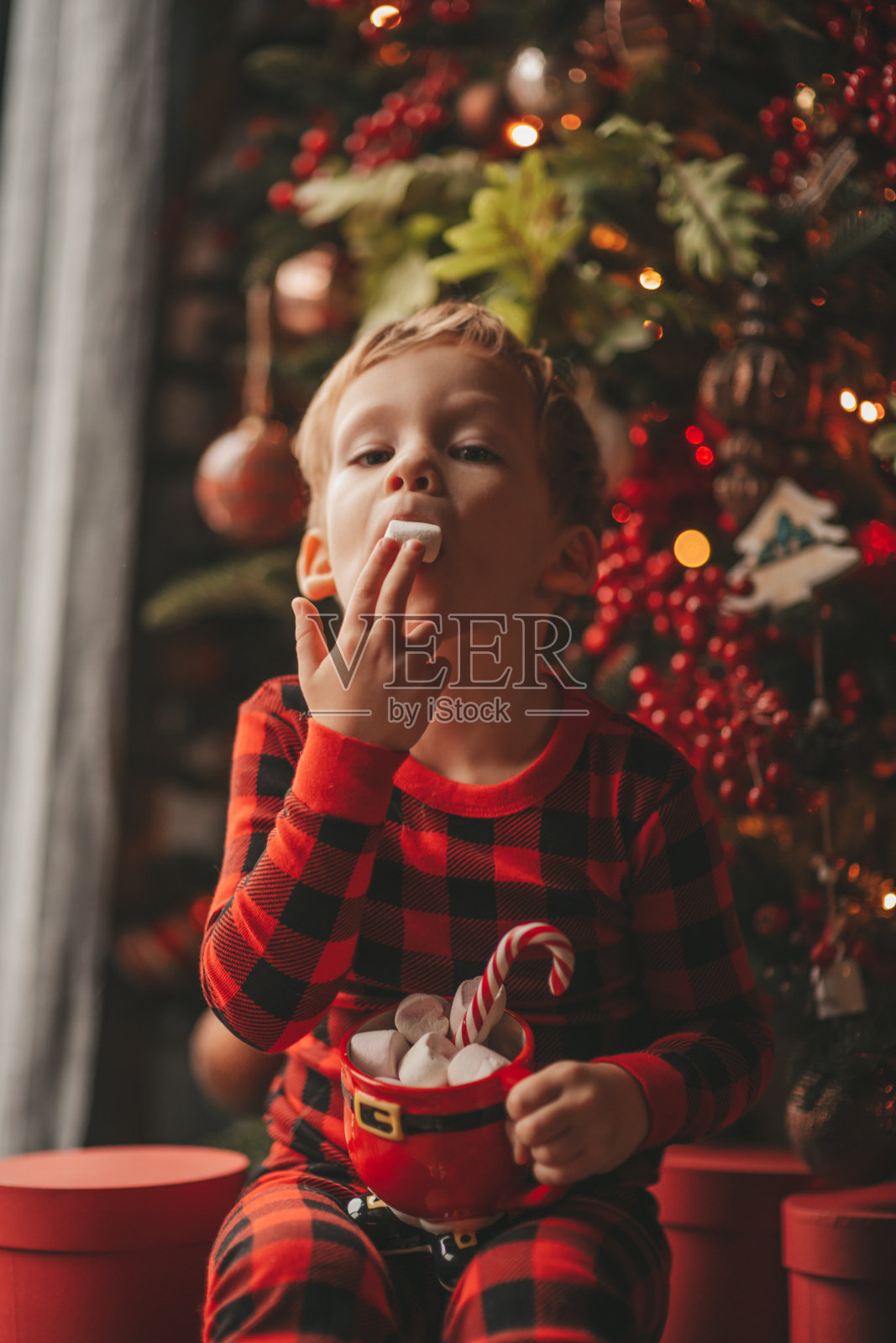 肖像偷拍快乐的孩子在红色格纹睡衣拿着圣诞马克杯棉花糖和拐杖糖照片摄影图片