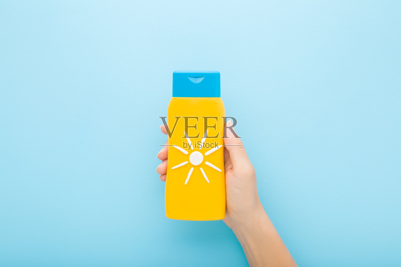 年轻的成年女性手拿黄色的防晒霜管在浅蓝色的背景。柔和的颜色。由白色奶油创建的太阳形状。夏天注意身体皮肤的保护。特写镜头。自顶向下视图。照片摄影图片