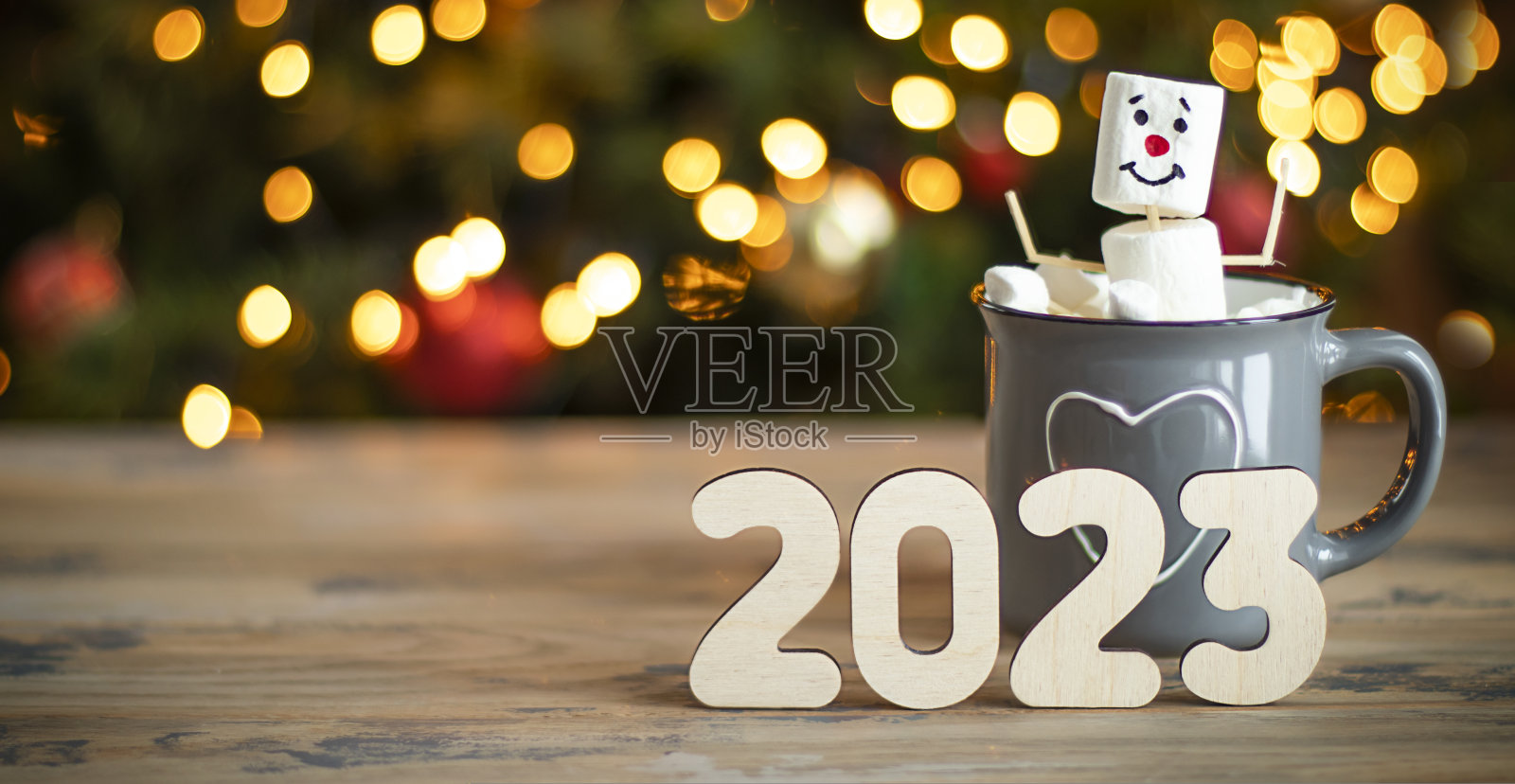 一个棉花糖人坐在圣诞树背景的可可杯里，数字是2023照片摄影图片