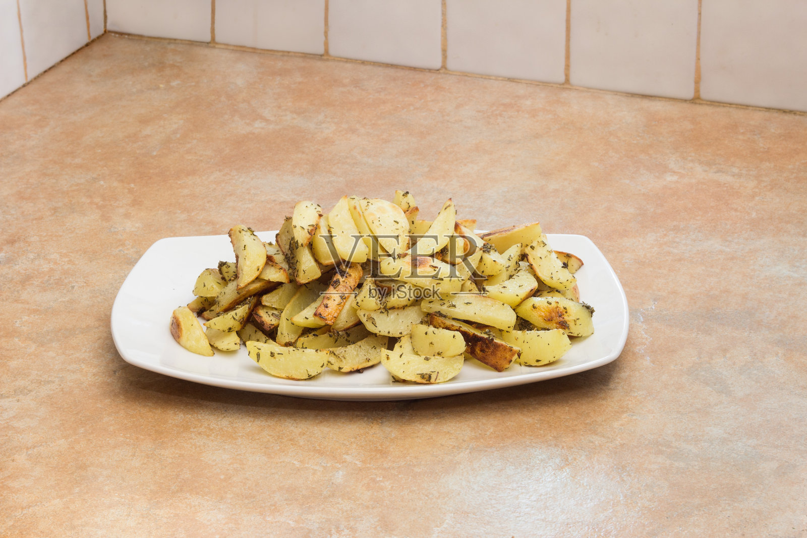一个白色的陶瓷大浅盘里盛着烤迷迭香土豆，放在质朴的石头和瓷砖厨房里。照片摄影图片
