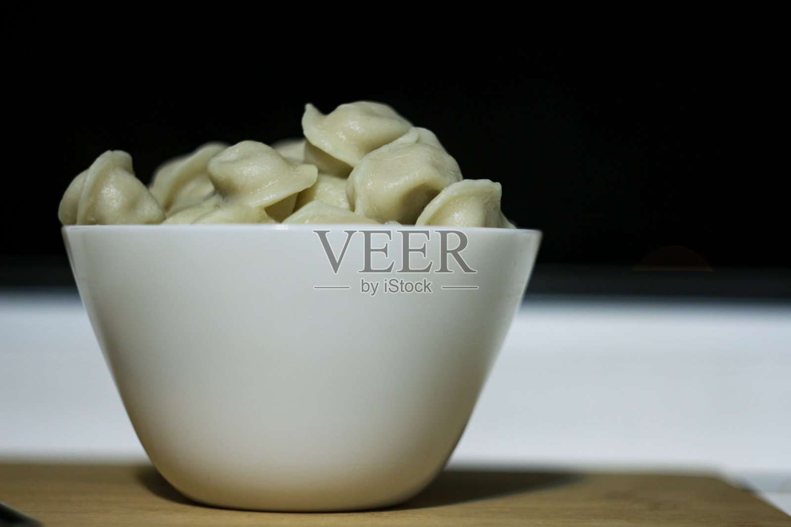 白色的碗里有新鲜煮好的饺子，背景是深色的照片摄影图片