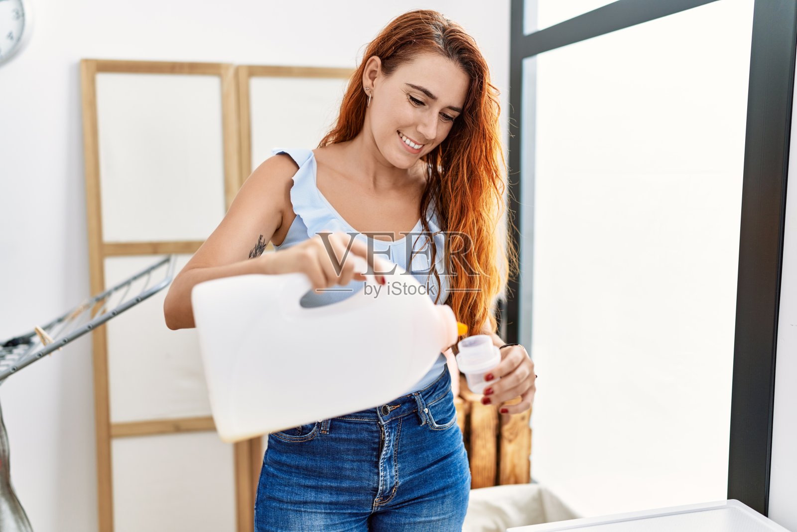 年轻的红发女子微笑自信地在洗衣房使用洗涤剂照片摄影图片