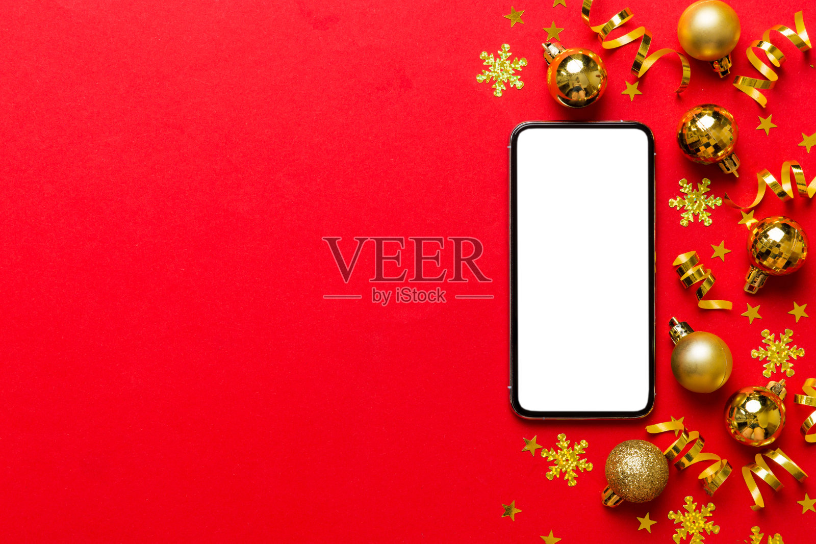 在家用手机进行圣诞节线上购物，顶部显示空白白色屏幕，智能手机在彩色背景上带有圣诞装饰球和复制空间，冬季假日促销背景照片摄影图片
