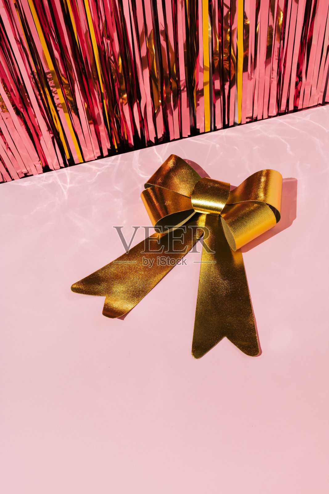 金色蝴蝶结在粉色背景与闪亮的圣诞金箔。新年问候概念。照片摄影图片