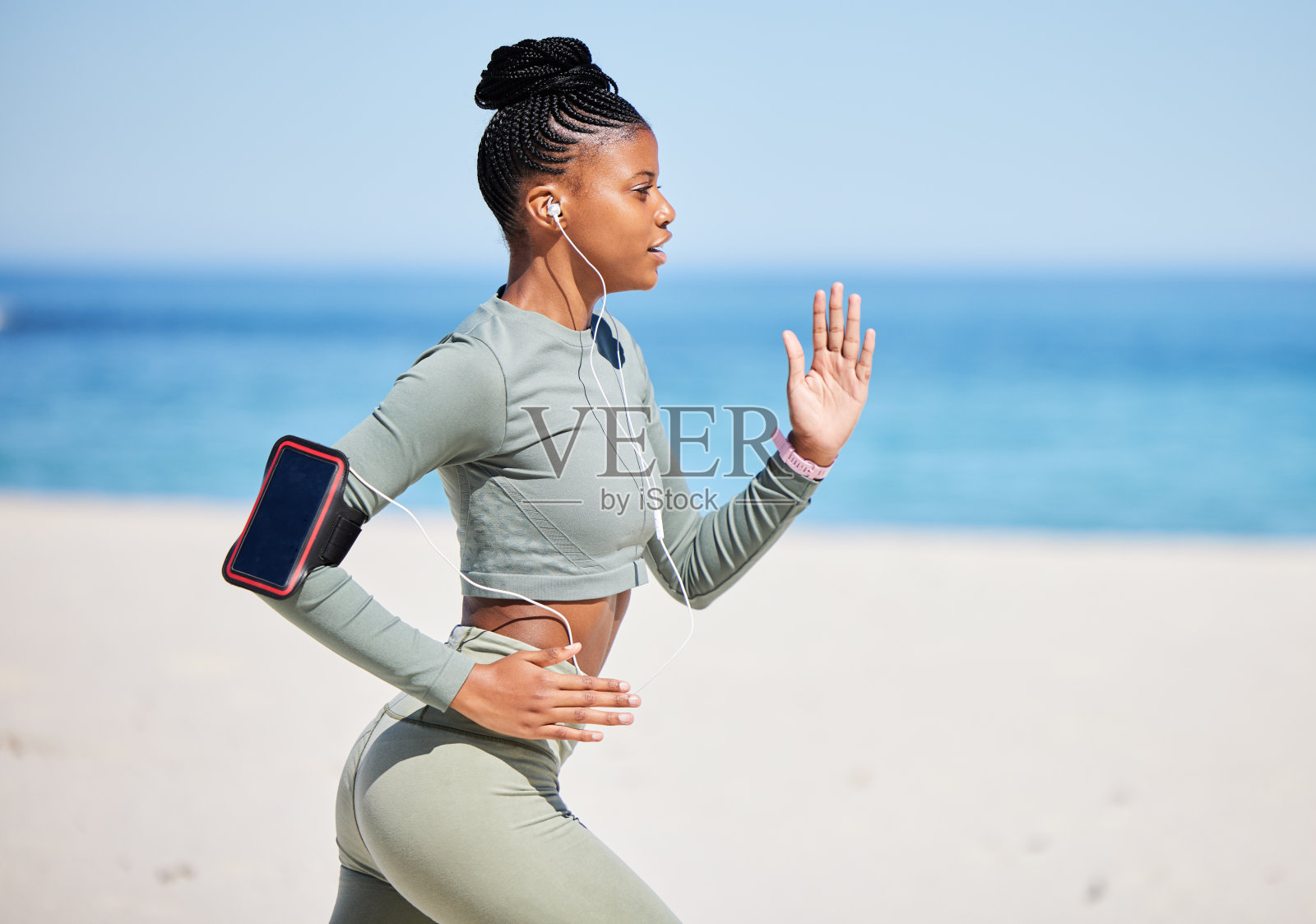 健康和活跃的非裔美国女性通过耳机听音乐，独自在海滩上跑步锻炼。关注黑人运动员的训练、锻炼和使用手机跟踪进展照片摄影图片