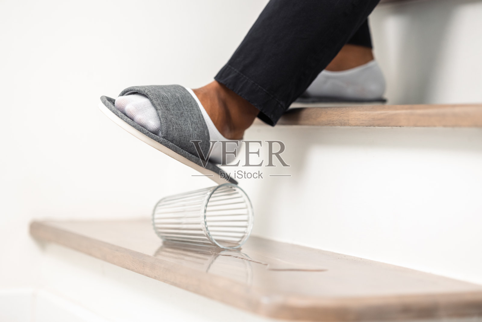 放在楼梯上的一杯水洒了出来，有发生事故的危险。那个年轻人正要踩到水面上，却滑倒了，受了伤。照片摄影图片