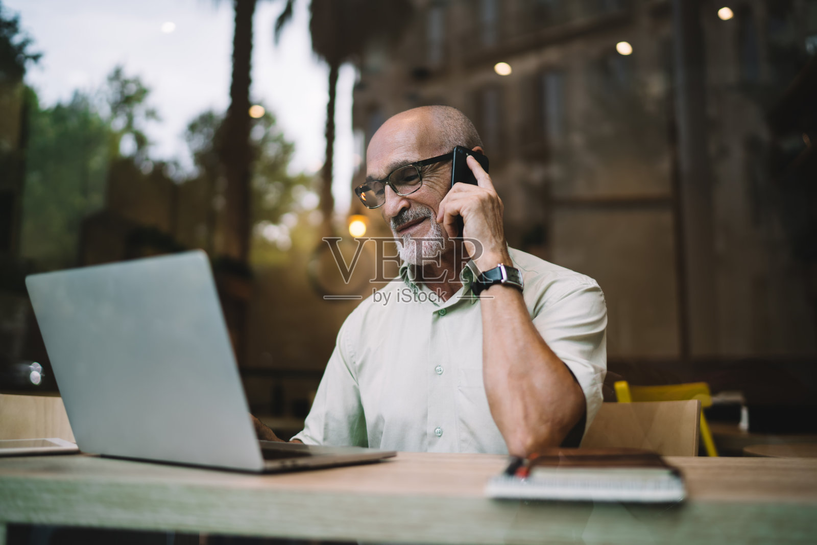 微笑的商人拿着笔记本电脑在咖啡馆里用智能手机聊天照片摄影图片