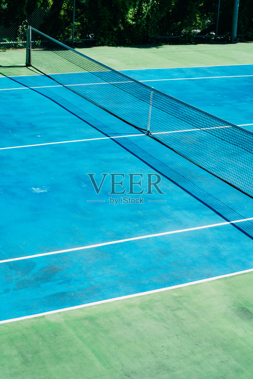 在一个阳光明媚的夏日早晨，公园里一个废弃的网球场，背景是绿树照片摄影图片