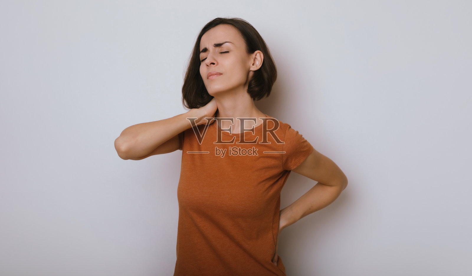 女性背部的脊髓有问题。慢性背痛。年轻的褐发女子正抱着她的下背部和脖子，站着忍受着难以忍受的剧痛。脊柱骨质疏松症。照片摄影图片