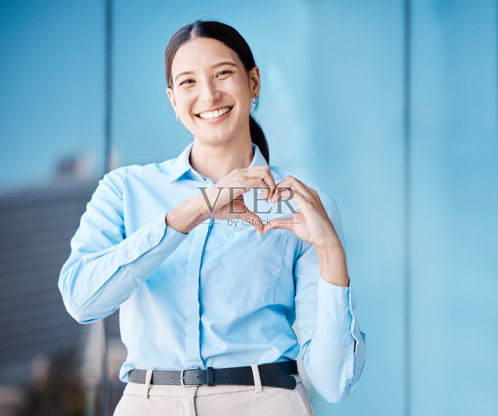 心，爱和健康的双手与商业妇女做一个手势与微笑在城外的城市。一名公司女员工独自站在户外示爱照片摄影图片