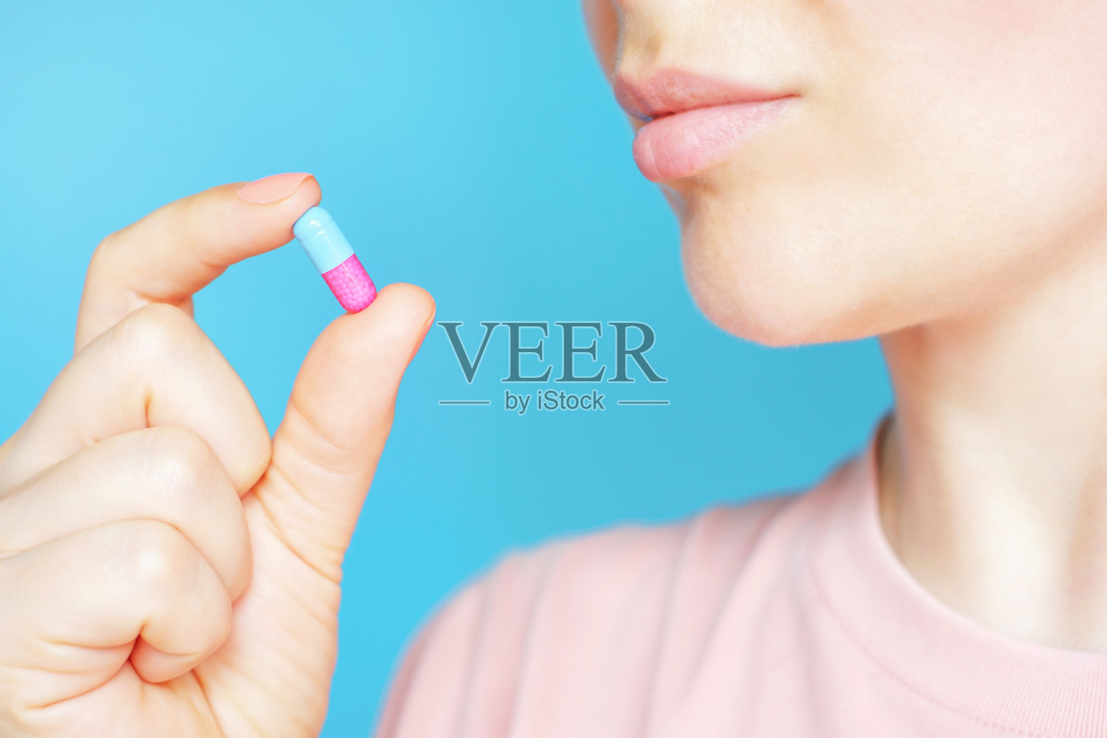 一个年轻的女人拿着一个胶囊在一个蓝色的背景特写。照片摄影图片