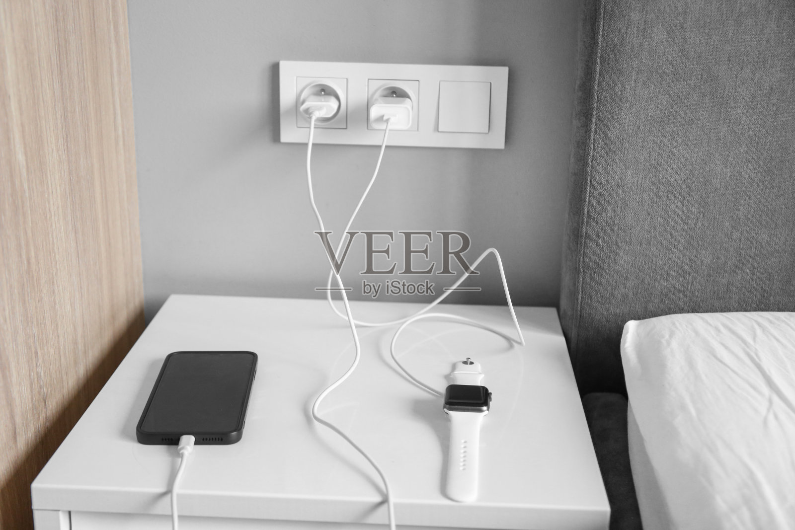 卧室里有充电的设备，床头柜上有充电的智能手表和手机照片摄影图片